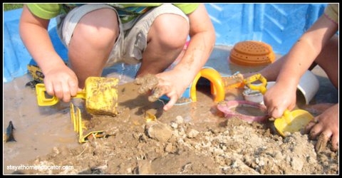 Playing with mud in a kiddie pool with shovels and rocks.