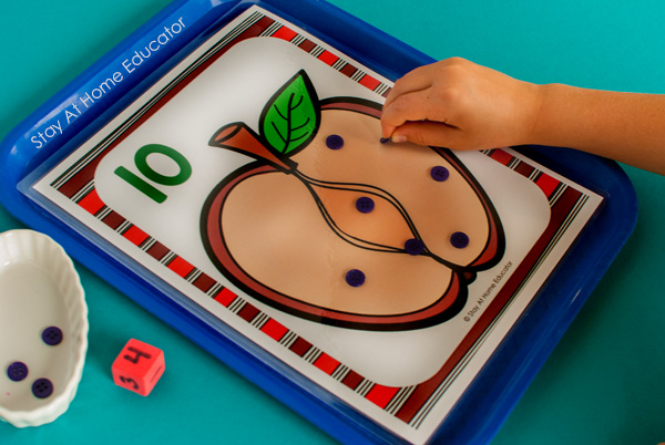a hand takes away an apple seed from a counting mat as a preschool addition and subtraction activity