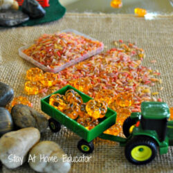 a toy tractor filled with dyed rice and acrylic pumpkins in a small world play setting