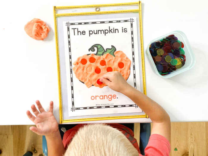 pumpkin colors | pumpkin booklets for preschoolers | pumpkin activities | a child smooshes orange playdough to cover the orange page of the pumpkin colors booklet, child then pushes orange counters into the playdough to do more color matching