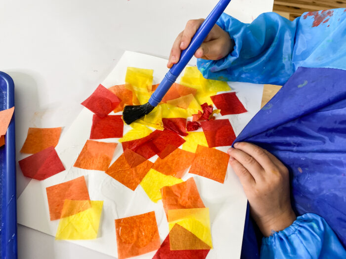 small hands painting glue onto tissue paper and enjoying fall activities for preschool