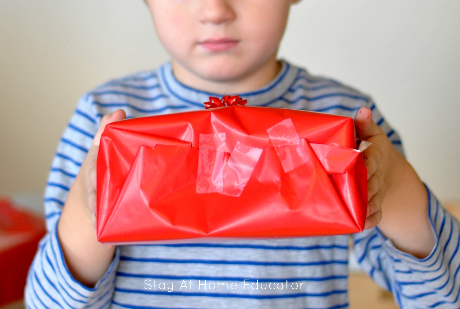 Christmas fine motor gift wrapping center | fine motor centers for preschoolers | preschooler holding up a gift that was wrapped at the fine motor center for Christmas theme