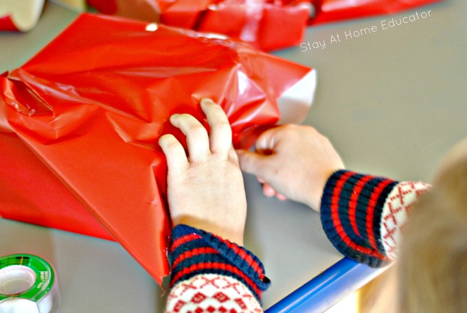 Christmas gift wrapping center for fine motor practice | Christmas fine motor gift wrapping center | preschooler using gift wrap and tape to wrap a pretend gift to work on self help skills and life skills