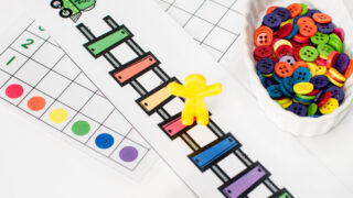 rainbow train tracks laid out with a yellow piece on the red track with a small bowl of rainbow buttons and a dice | rainbow preschool activities | counting activities for preschool |