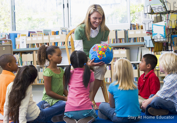 Kindergarten teacher and children looking at globe in library as part of lesson plans for preschool 