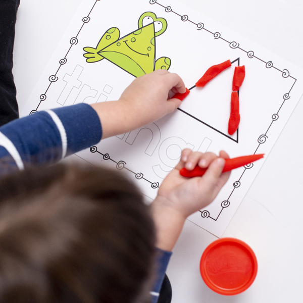 A boy learning about shapes for preschoolers by putting playdough onto a triangle shape mat