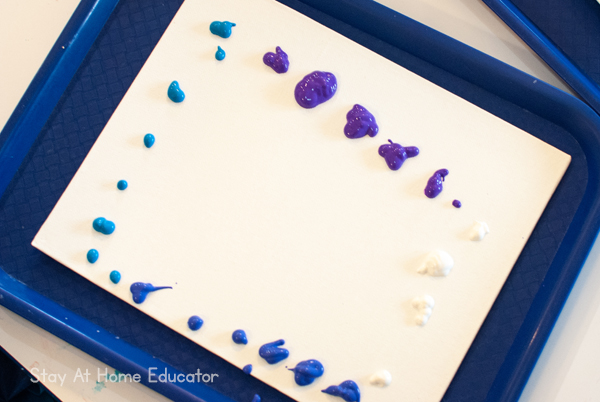 Winter process art for preschoolers, start by adding drops of paint to a canvas.