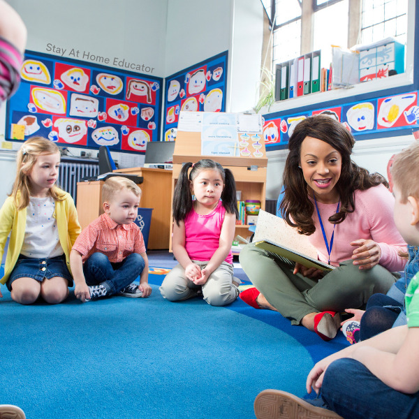 a preschool teacher sitting on the floor with her students while following  the best preschool schedule