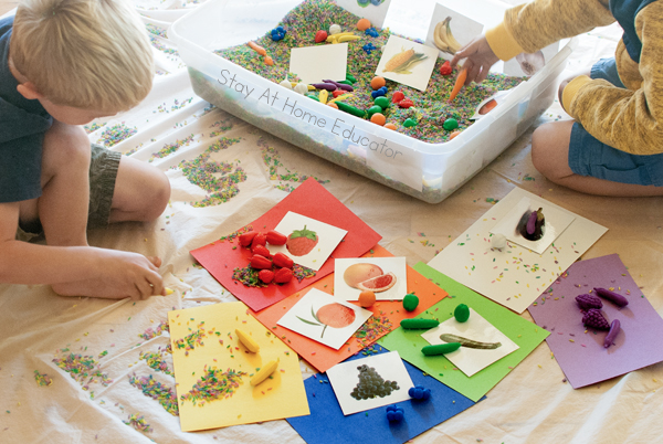 Fruit and veggie sensory bin for preschoolers| image shows plastic bin with colored rice, mini fruit and veggie manipulatives and corresponding cards| Image includes different colored papers used as sorting mats with corresponding fruits, veggies, and cards|