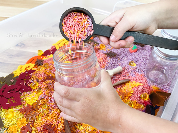 a child practicing his scooping and pouring skills with colored rice into a sensory bin for preschoolers.