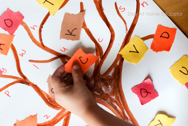 fall tree craft for preschoolers| a child's hand holds up a capital letter C written on construction paper to look like a tree leaf as he matches uppercase letters to lowercase letters on the tree paper| torn papers are red, orange, yellow, and brown| alphabet tree activity and craft|