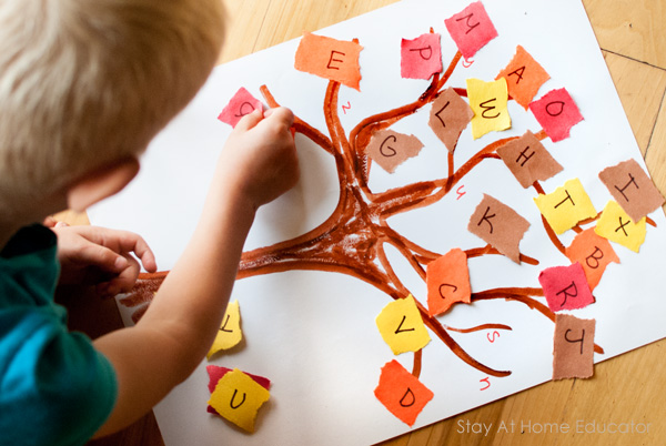 fall tree craft for preschoolers| a preschooler is shown securing uppercase letters written on torn colored papers onto the matching lowercase letters on the tree paper| torn papers are red, orange, yellow, and brown| alphabet tree activity and craft|