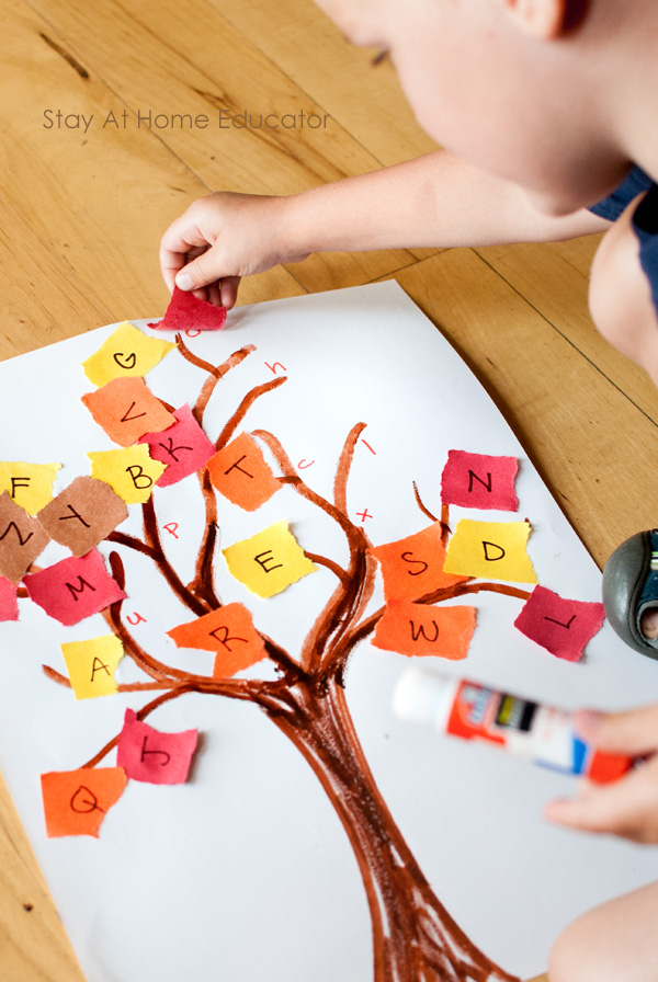 fall tree craft for preschoolers| a preschooler is shown with a glue stick, gluing uppercase letters written on torn colored papers onto the matching lowercase letters on the tree paper| torn papers are red, orange, yellow, and brown| alphabet tree activity and craft|