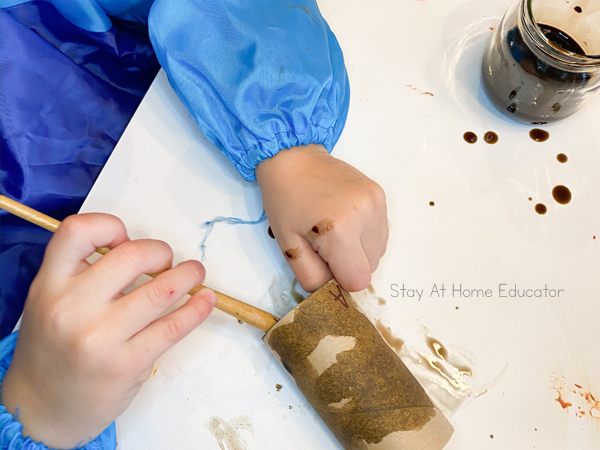 a preschool hand painting a cardboard tube brown in preparation for a paper plate turkey craft