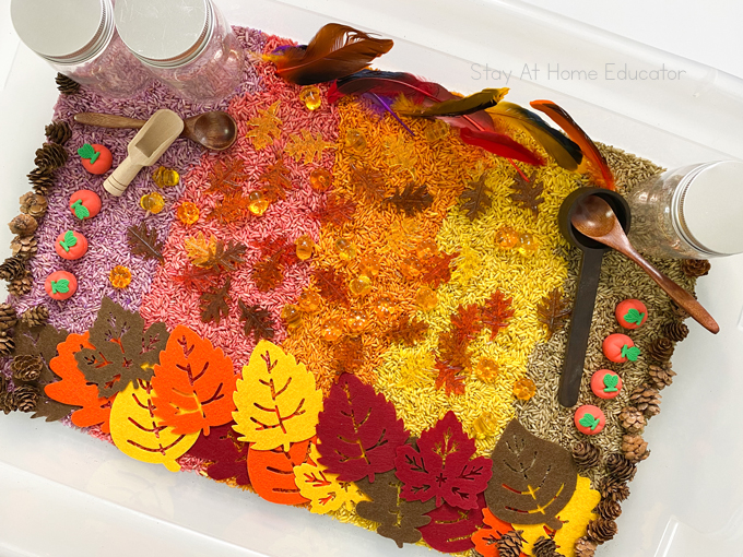 a fall sensory bin for preschoolers that's filled with colorful dyed rice, iconic fall items, scoops, and jars