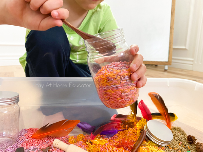 a preschooler who has almost filled a glass jar with colorful fall rice
