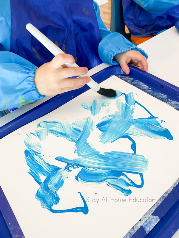 a preschool hand painting a canvas light blue as the first step of their Christmas process art activity