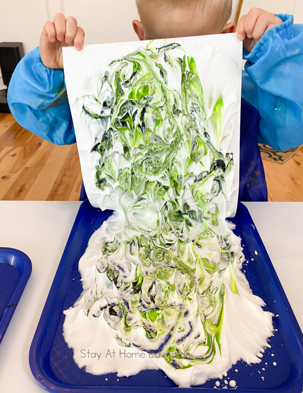a preschool child lifting a piece of cardstock off of marbled shaving cream while he makes a winter craft for kids