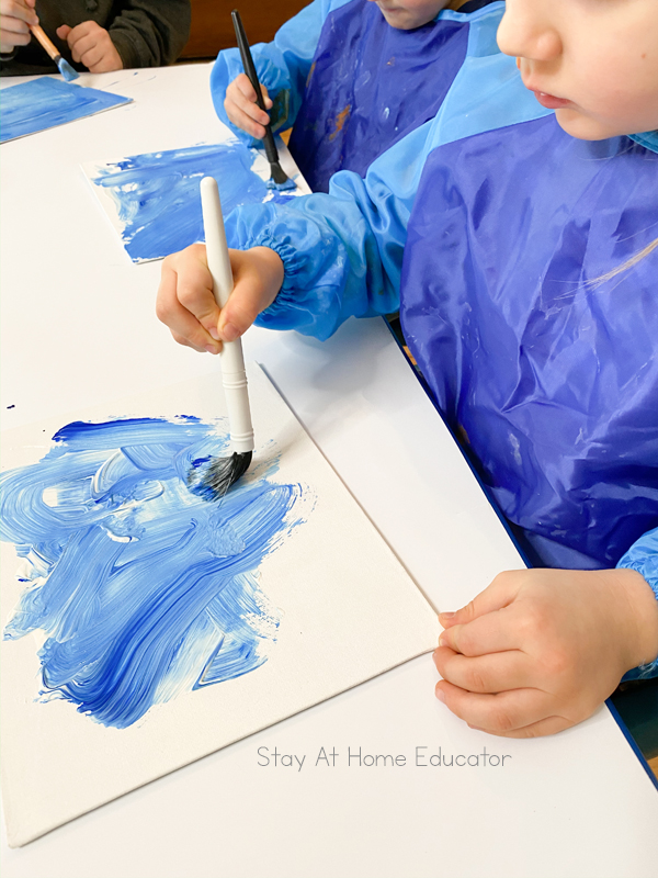 students mixing blue and white paint to make a wintery background for their snow themed art project for preschoolers