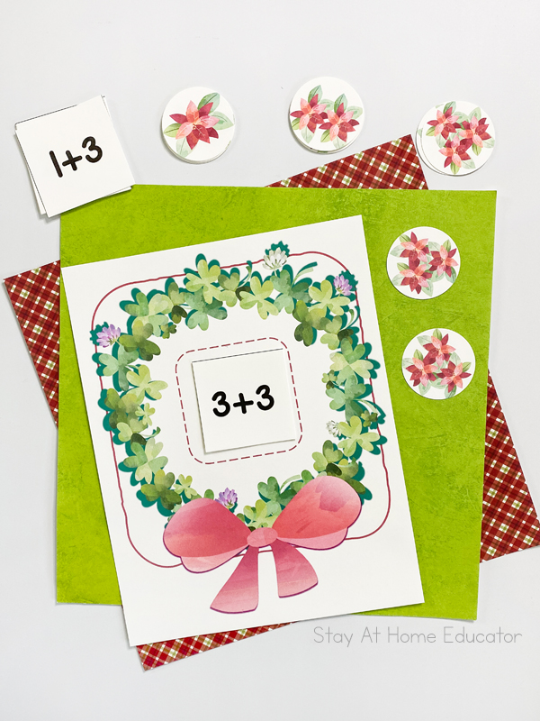 a free printable wreath addition mat with the addition fact 3+3 on it and two poinsettia cards with three flowers each on the wreath