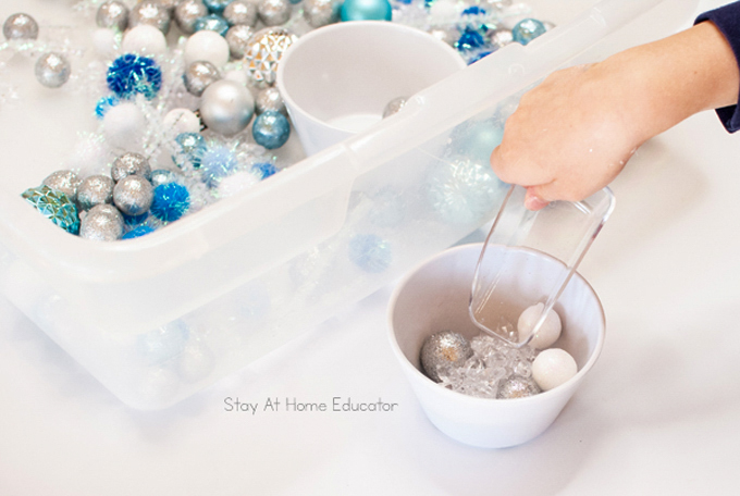 a child scooping objects from the winter sensory bin into a nearby bowl