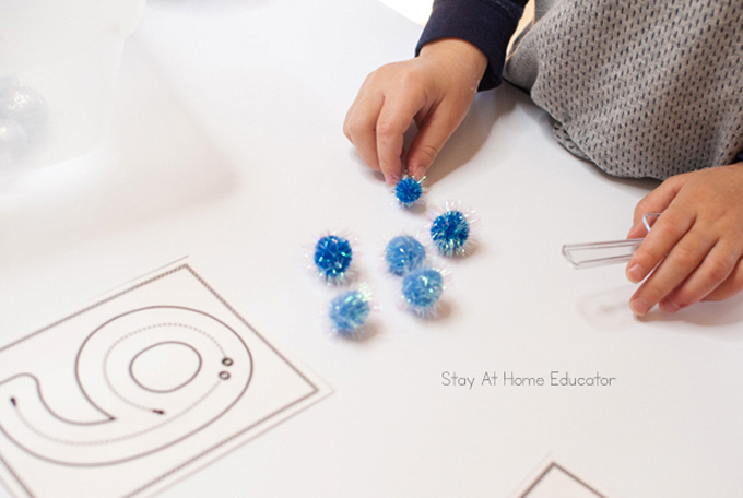 a child counting out 6 blue pom-poms from their winter sensory bin to match the number formation card.