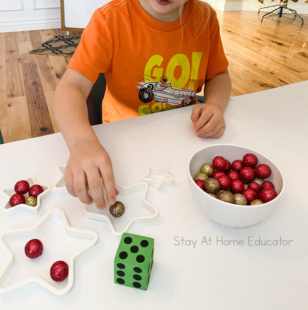 a child is adding one sparkly ball to a star shaped cookie cutter as part of a preschool christmas math game
