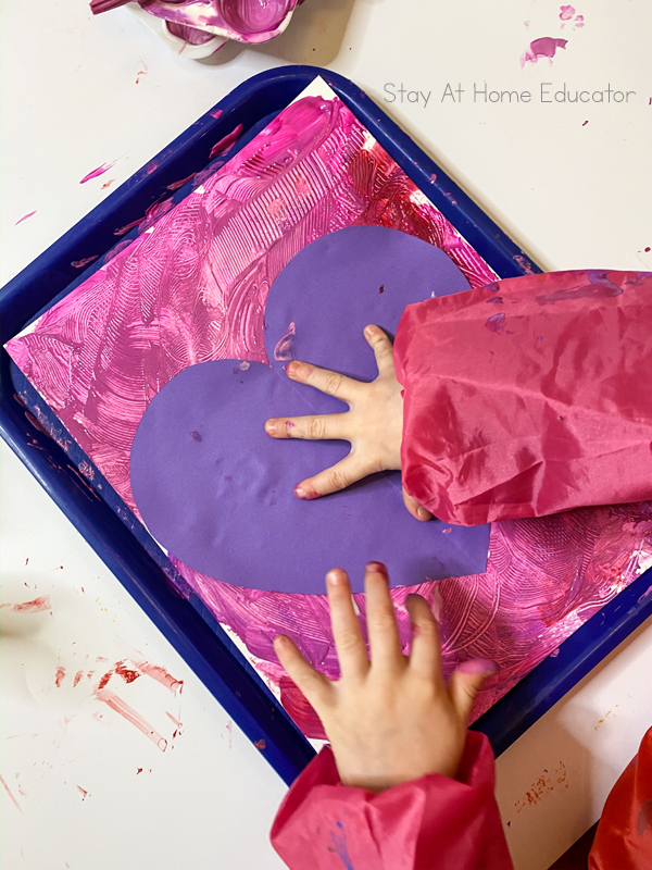 a small preschool hand pressing a heart onto their valentine's day craft