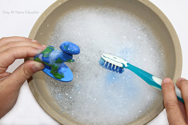 a painted dinosaur is being scrubbed with a soapy water and a toothbrush in this dinosaur activity for toddlers