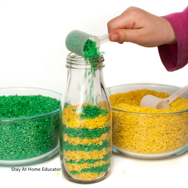 a preschooler's hand layers green and yellow rice into a jar while completing preschool pattern activities