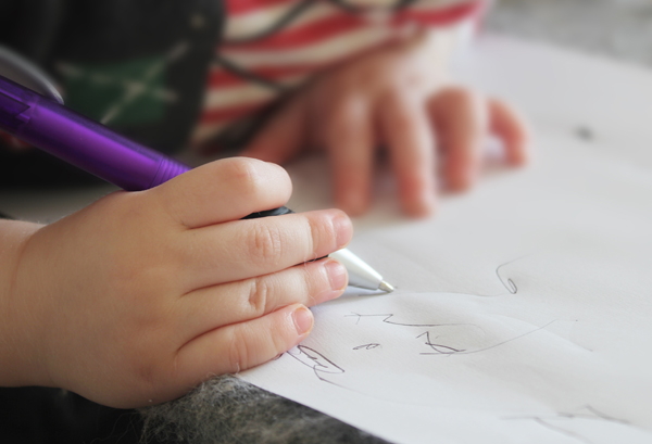 A young child makes deliberate lines on a paper as part of writing development in preschool