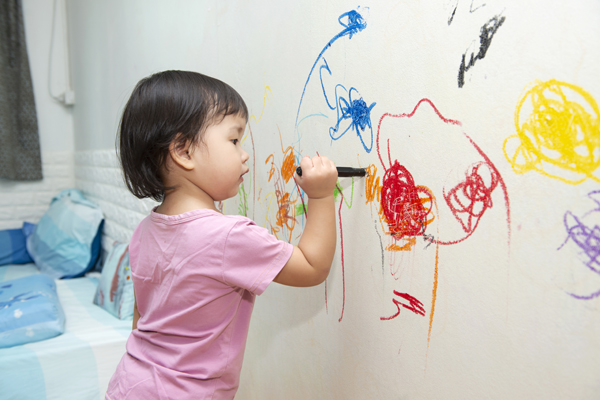 A young girl scribbles on a wall covered in butcher paper during preschool writing activities