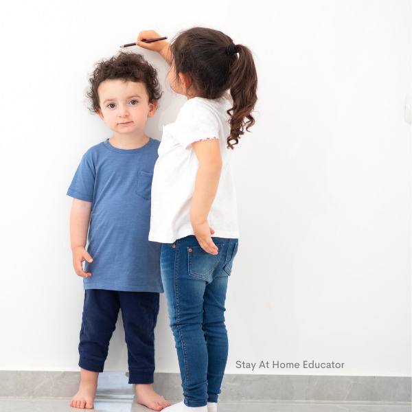 A young girl measuring her younger brother as part of preschool measurement activities