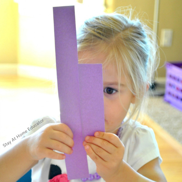 a young girl comparing two different lengths of paper as part of an activity of measurement of length