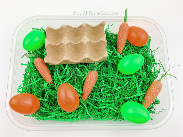 an easter sensory bin filled with orange and green materials like plastic eggs and carrots