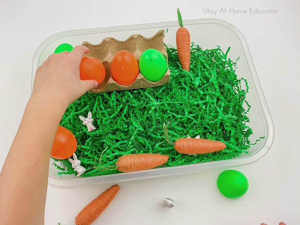 a child's hand plays with plastic eggs in an Easter sensory bin