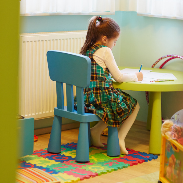 a preschool girl writes at a colorful school table while working on name writing activities