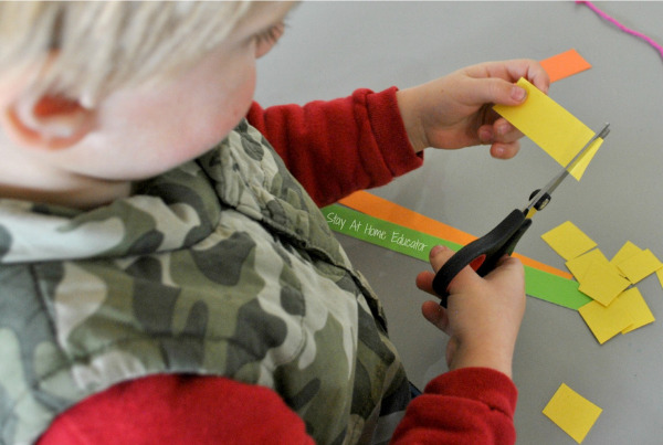 a young boy completing scissor cutting exercises for preschoolers by cutting a strip of paper into small pieces