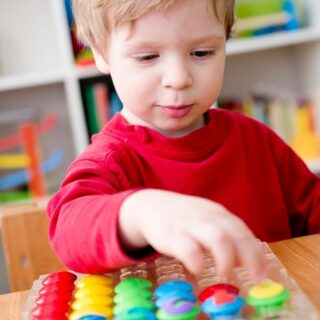 young boy sorts pegs by color after his preschool lesson plan on sorting and comparing
