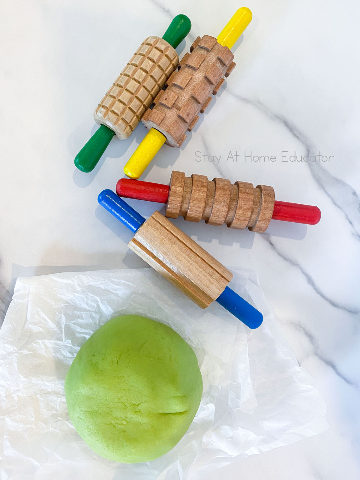 Looking for a recipe for cooked playdough? This cooked playdough recipe is easily the best because it is soft playdough that lasts a long time. Playdough on parchment paper with playdough rolling pins.