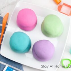 easiest ever playdough recipe super soft | fun and easy activity | four playdough in one white plate : color neon - pink, classic blue, purple, green with gel food coloring, cookie cutters and playdough tools | super easy, no-cook easy playdough recipe! | soft, colorful, and endlessly moldable