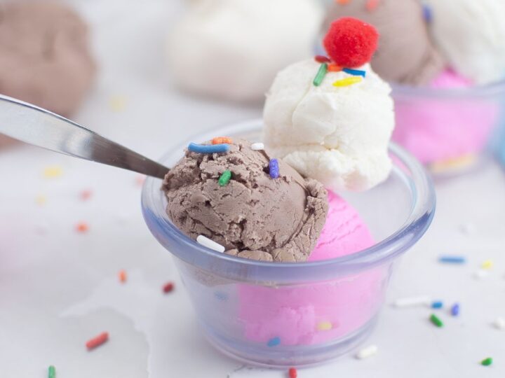 A colorful picture of a sundae dish filled with ice cream playdough that looks just like real Neapolitan flavors, with layers of chocolate, vanilla, and strawberry. This playful playdough recipe, which looks and scoops like real ice cream, is a fun and educational activity, great for teaching preschoolers about ice cream.